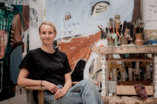 Girl with blonde hair and black t-shirt sitting in artist studio. Zoe Grey.