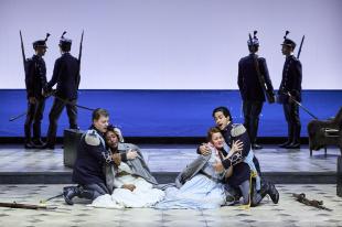 Four soldiers in shadow standing in pairs in the background. In the foreground are two soldiers, crouching on the ground, each one holding a woman in his arms. The women are wearing white gowns.