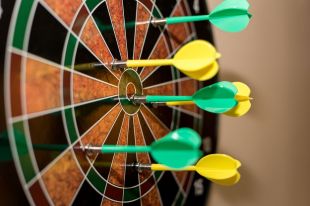 A colourful photograph of yellow and green darts embedded in a dart board.