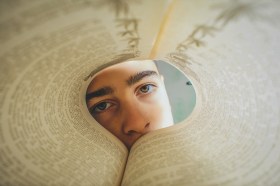 Prime Minister's Literary Awards. The eyes and nose of a boy is seen through the circular fold up pages of a book.