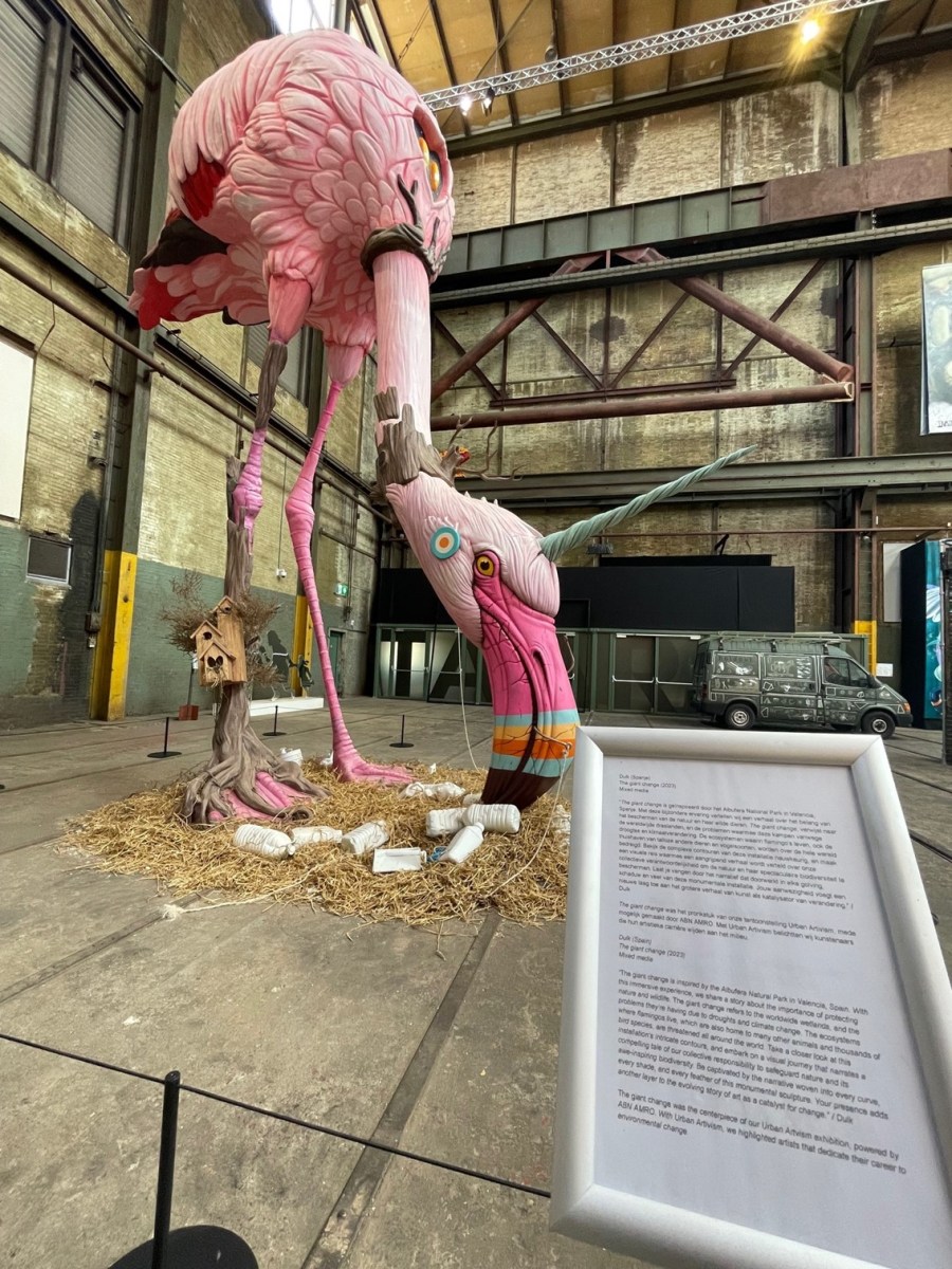 Culture. A large artwork of a flamingo in an urban space is pecking at litter.