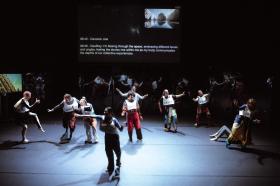 A group of dancers are performing in 'Plagiary'. There is text above them as they dance.