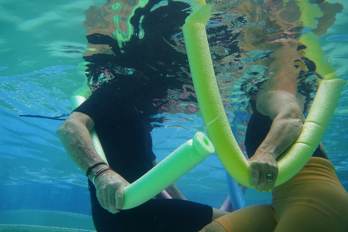 Work from Gold Coast artist Kathy Mackey, on show at HOTA. Image depicts the bodies of two people underwater, holding swimming noodles.