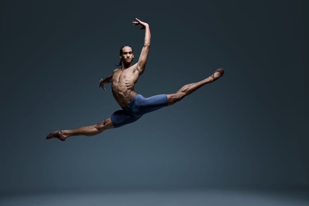 The Australian Ballet's soloist, Davi Ramos, in a promotional image for company's 2025 season. A shirtless male ballet dancer is photographed mid-leap, his legs outstretched and arms raised dramatically.