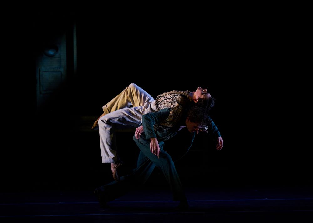 Benjamin Garrett and Callum Linnane in The Australian Ballet's 'Oscar', in a scene where Oscar Wilde (Linnane) wearing a drab prison uniform is bent over and carrying the splendidly dressed Bosie (Garrett) upon his bowed back.