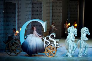 A scene from 'Cinderella' ('Cendrillon') at Royal Opera House 2011; Laurent Pelly’s production has been programmed as part of Opera Australia's 2025 Sydney season. Four performers in horse costumes draw a carriage shaped like the letter C, in which a woman in a white ball gown is singing.