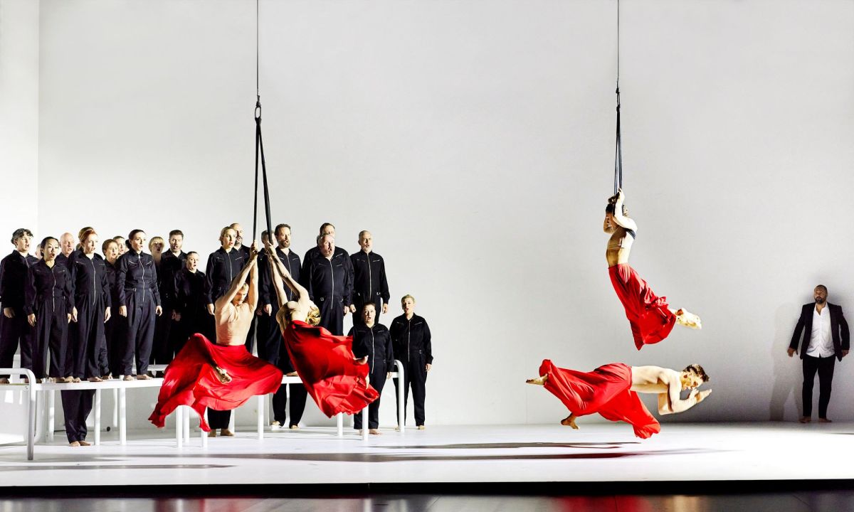 Gluck's 'Orpheus & Eurydice' will be staged in Melbourne in 2025. Pictured is the Opera Australia Chorus and Circa in Opera Australia's 2024 production of 'Orpheus & Eurydice'. Four male circus performers, shirtless and wearing vivid red skirts, swing and tumble on a stark white stage, as formally-clad opera chorus members sing behind them.