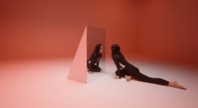 Dancer in black body suit on floor, looking into mirror in pink toned room. Amrita Hepi.