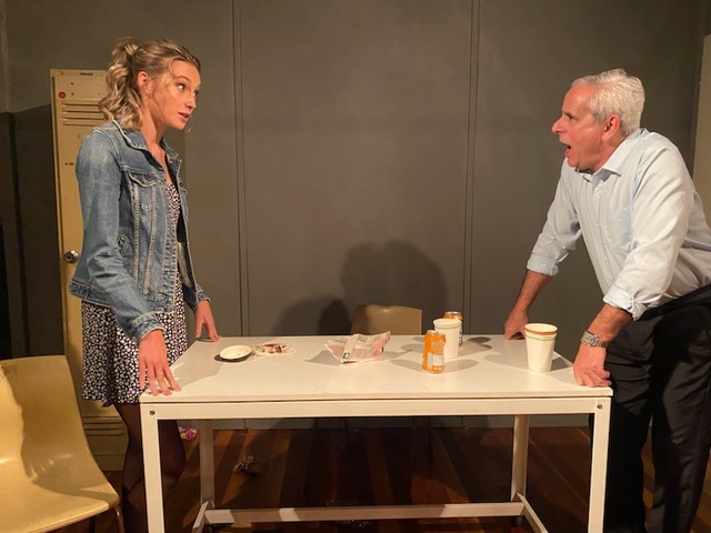 A young blonde woman in denim jacket (Ashleigh Hermann) is staring across a table at an older man (Daniel Mitchell) in 'Blackbird.'