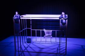 In a blue-lit stage, two young men, Nelson Clay and Corey Saylor-Brunskill, are standing on a box-like structure.