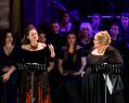 Two leading women opera singers (Deborah Humble and Helena Dix) in black with a chorus on singers in the background. Puccini.