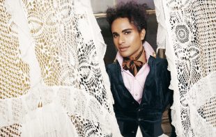 Venezuelan-born male soprano Samuel Mariño opens the Australian Brandenburg Orchestra's 2025 season. Wearing a green velvet waistcoat, a pale pink shirt and a cravat, Mariño - who has light brown skin, dark eyes and curly black hair - parts a pair of white lace curtains and gently smiles at the camera.