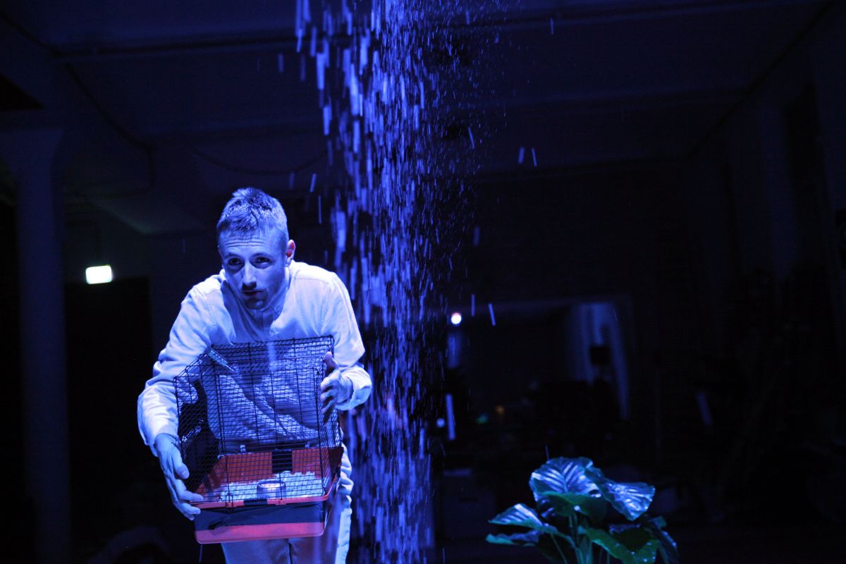 in a blue tinged photo a man is showing the contents of a small cage like tray in front of him. Disaster.