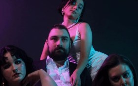 A bearded man is sitting in the middle surrounded by three women in the production of 'Don Giovanni.'