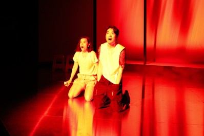 A scene from the STC season of 'Golden Blood'. Photo: Prudence Upton. Two Asian-Australian actors, a young woman and a young man, kneel on an orange-lot stage.