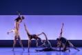 Six dancers are in various bodily formations. The light behind them is a light blue. Twofold.