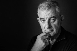 Greek-Australian actor, director and advocate Lex Marinos has died aged 75. The photo shows Marinos in a thoughtful pose. his grey hair short, his face lined and his right hand rested contemplatively on his chin.