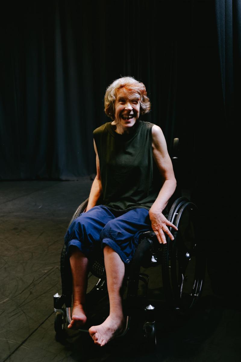 A middle aged woman in a wheelchair with a sleeveless black top and rolled up blue trousers is one stage. Melinda Smith.