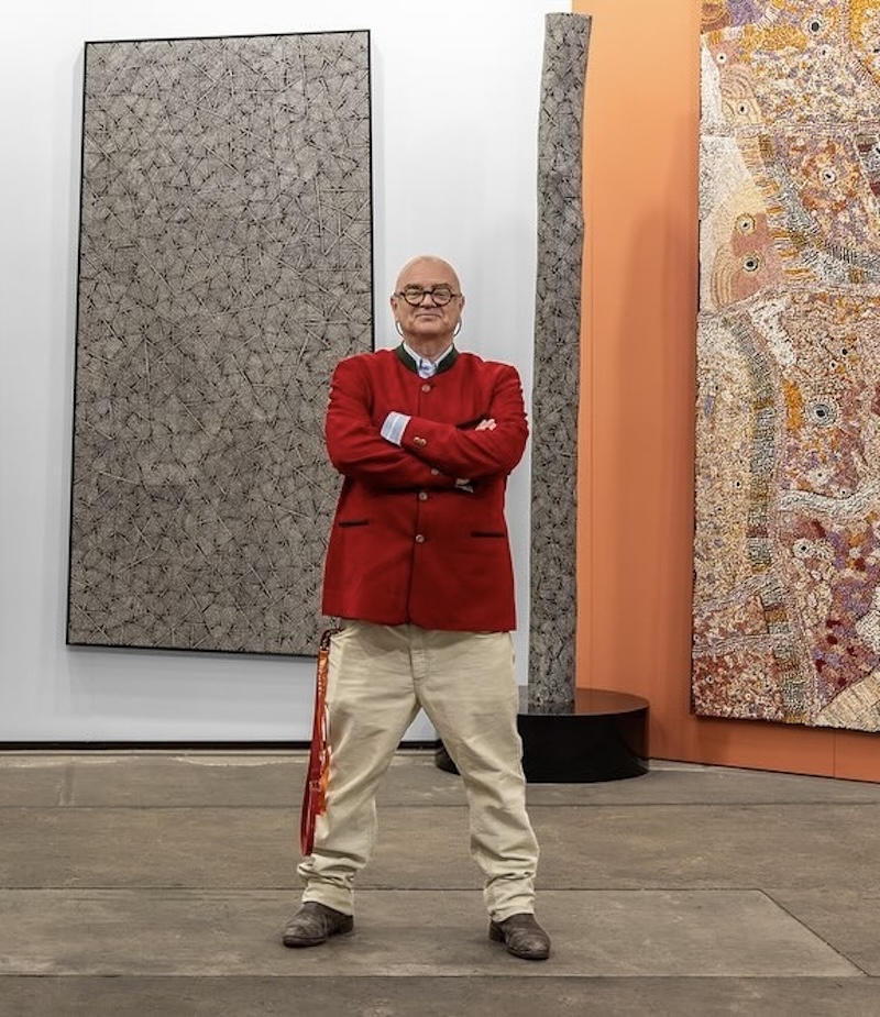 Older man with glasses standing wearing red jacket and arms crossed in art fair setting. Michael Reid.