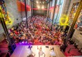 Crowd dancing within art gallery, with colour flags and lights. NGV Indian Community Day