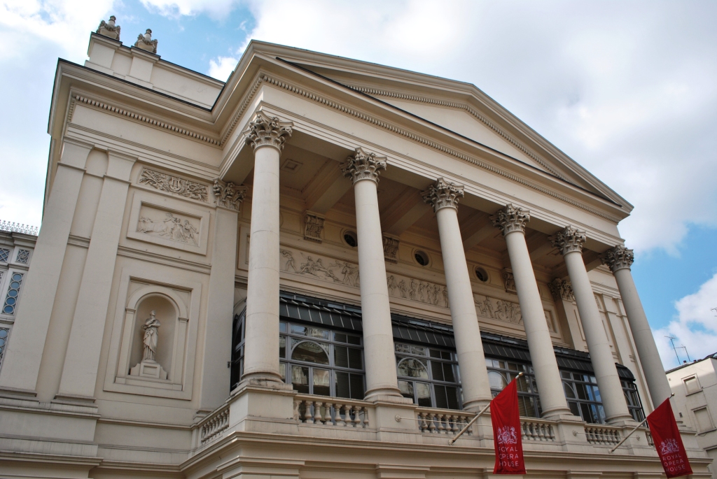 Royal Opera House. The facade of a grand London building, with five pillars and red banners.