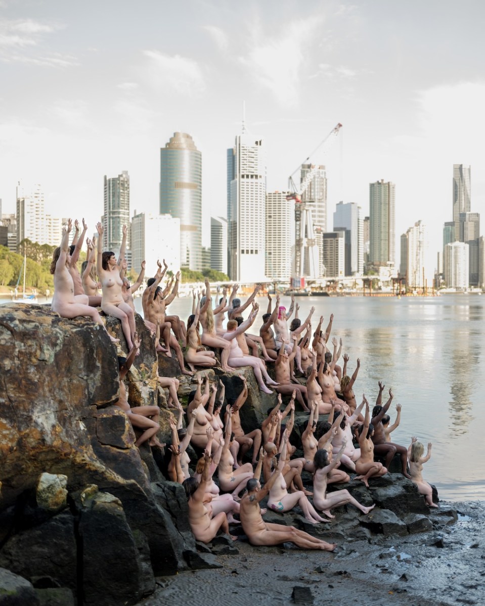 Group of naked people sitting on rive edge is city setting, Spencer Tunick, Brisbane.