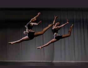 Two female dancers leaping on stage. Tara Gower