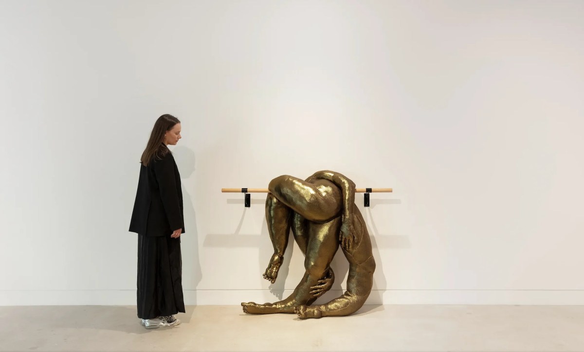 Woman in black standing next to a wall mounted gold soft sculpture on ballet barre. Tarryn Gill