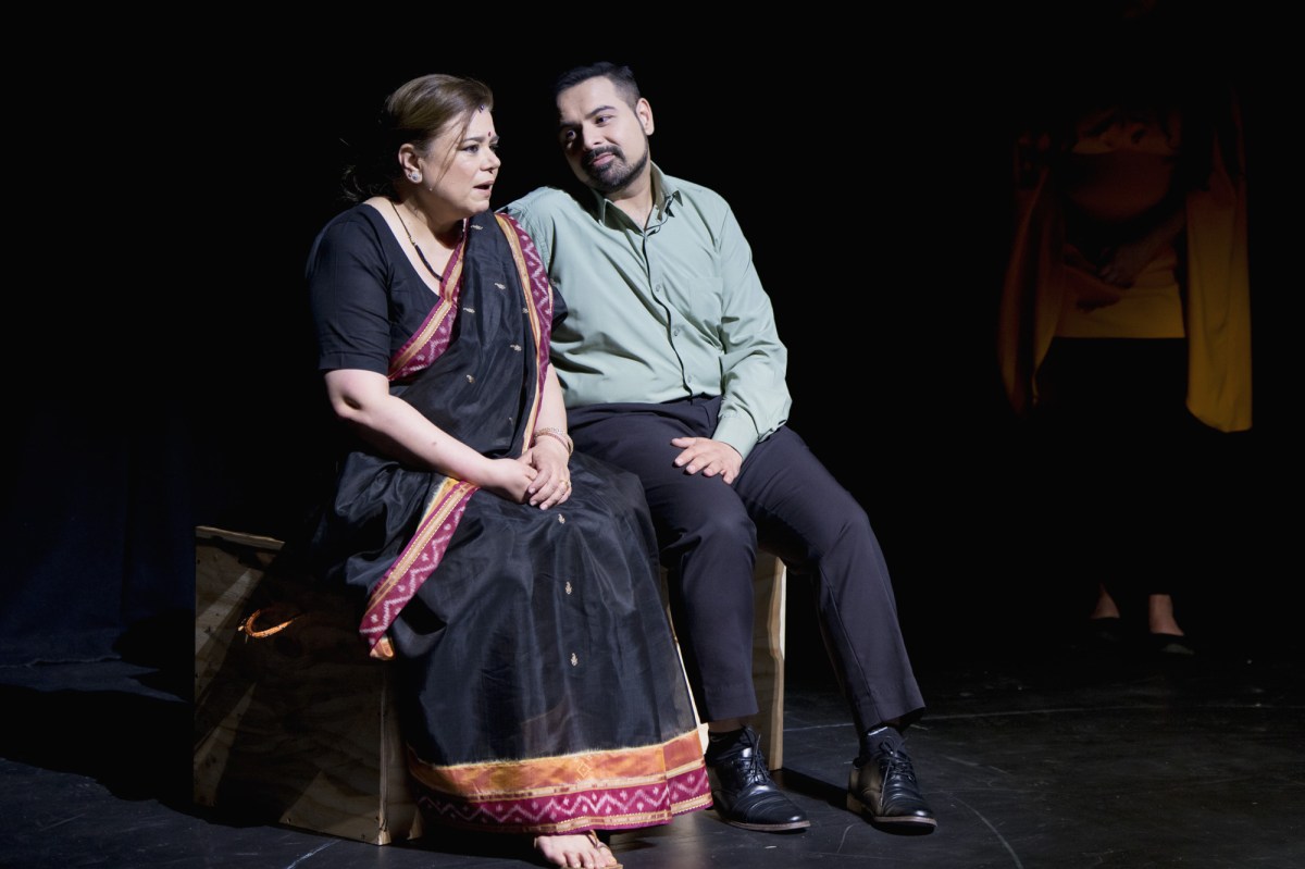 A woman in a sari is sitting next to a bearded man with a blue shirt and dark pants in the stage show of 'Ten years to Home.'