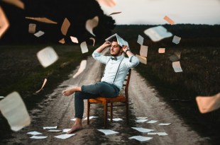 Man sitting on chair being showered by floating paper sheets. Arts news.