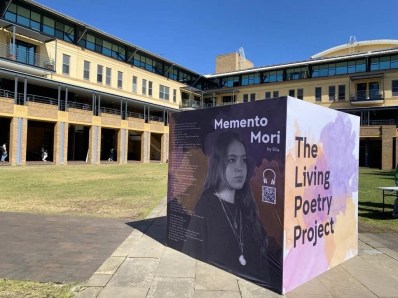 A block sculpture on university grounds. Two sides can be seen. One side says 'Mememto Mori" with a photo of a young woman. The other side reads 'The Living Poetry Project.'