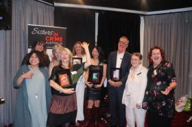 Sulari Gentill, Lucinda Gifford (F), Amy Doak, Alison Goodman, Christine Keighery, Monica Vuu, Andrew Harrison (representing Rebecca Hazel, Kelly Gardiner and Carmel Shute at Sisters in Crime's 24th Davitt Awards.A group of smiling women and one man hold books and prizes in front of a banner that reads Sisters In Crime.