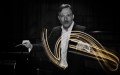 Black and white photo of QSO Chief Conductor Umberto Clerici waving his conductor baton. The swirls are depicted in yelllow.