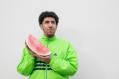 A Middle Eastern man in a green fluro top is holding a slice of watermelon.