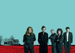 A promotional image for Black Swan’s 2025 production, ‘August: Osage County’. Five actors pose for the camera against a bacldrop formed by a bright red field and a blue sky. A tree-encircled family home is visible in the distance.