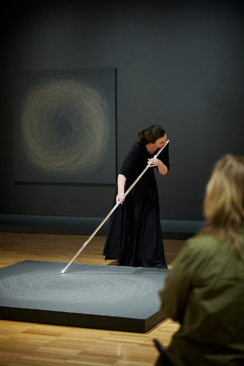 Woman dressed in black playing flute and making a drawing. Dobell Biennial