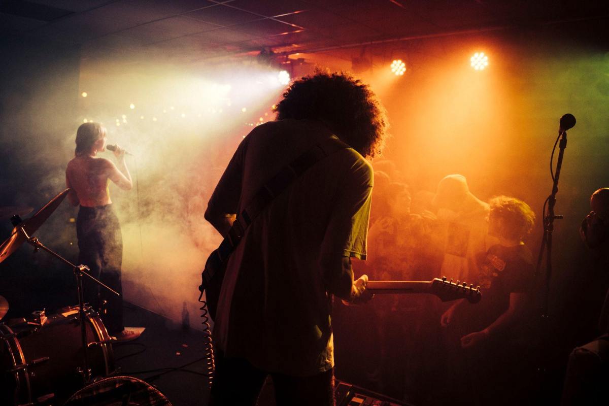 A curly haired rock guitarist shot from behind playing to a crowd bathed in orange light.