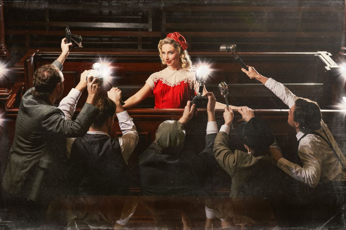 'A Modern Murder' at Sydney Festival is sure to be a 2025 program highlight. A blonde woman in a short-sleeved red dress and red hat smiles flirtatiously from the dock in an old-fashioned courtroom. A swarm of photographers and radio-men crowd around her.