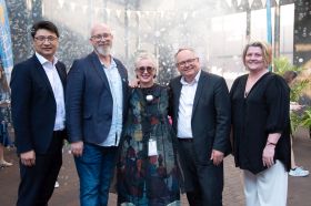 Barking Gecko Arts: five adult people, three male, two female, posing for a group photo at an event in an outdoor courtyard setting.