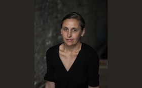 Portrait image of choreographer Anne Teresa de Keersmaeker. The face and shoulders of a European woman in her forties looking into the camera.