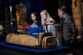 three people leaning over a museum case looking at ancient Egyptian artefacts.