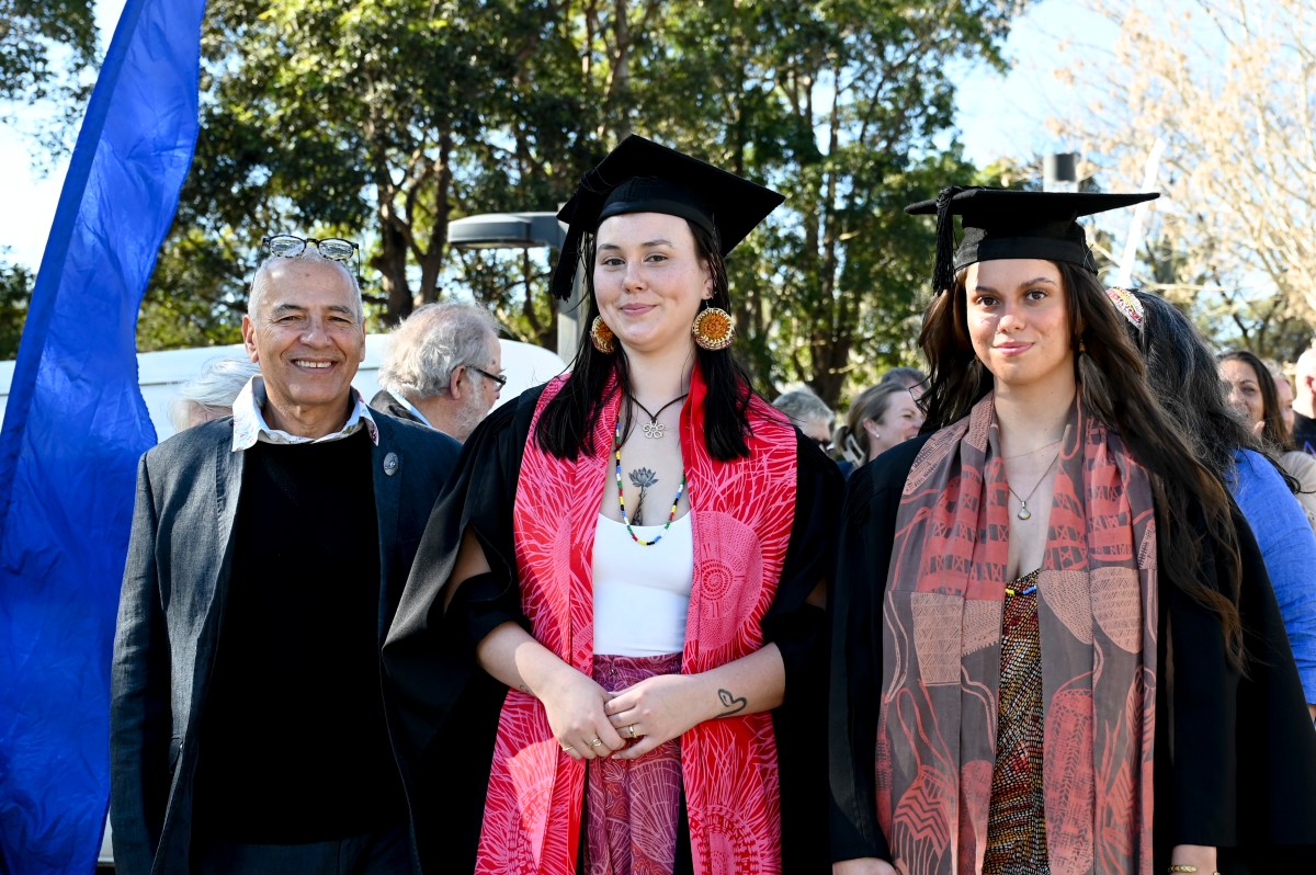 NAISDA CEO Kim Walker (an senior man with light brown skin and short white hair, smiling) with NAISDA Graduates Peta-Louise Rixom (a young woman with pale skin,should length dark hair, wearing a black graduation cap) and Maddison Fraser (a young woman with light brown skin, brown chest length hair, wearing a black graduation cap), June 2024. First Nations graduates at NAISDA.