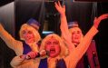 Ellen O'Connor, Kaia Reyes and Sophie Bengough are three young women dressed as airline stewards in white and blue. They have their hands in the air in a production of 'All the Things We've Done.'