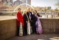 Four women in winter coats lean against a wall on the banks of the river Yarra. With Melbourne's Flinders Street station on the other side of the river. They all have instrument cases - two violins, one viola and a cello. Flinders Quartet