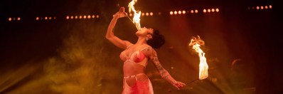 Heather Holliday, has her head back and is fire-eating in 'La Clique.' She is dressed in a red and white bikini top outfit.