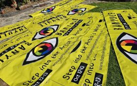 Street banners for the annual Banyule Open Studios weekend. Several bright yellow banners with the logo of a large rainbow eye at the centre, laying on the lawn. There is the tag line ‘Step into the Artists’ World’ and the dates ‘Oct 12-13’.