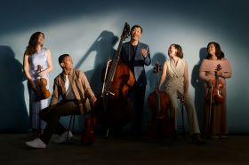 Adelaide Symphony Orchestra's 2025 season hero image. Five members of the Orchestra, three women and two men, pose casually against a blue wall with their instruments.