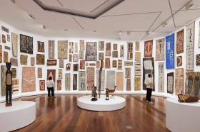 Visitors standing in gallery with floor to ceiling presentation of bark paintings. NGV