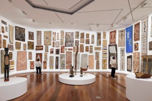 Visitors standing in gallery with floor to ceiling presentation of bark paintings. NGV