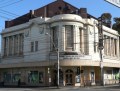 a heritage theatre building on the corner of two streets with many wires crossing in front of it. National Theatre